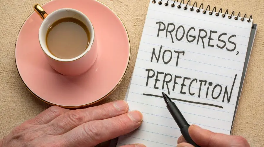 Progress not perfection is written on a notepad next to a coffee