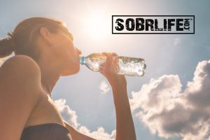 Drinking water in addiction recovery is essential: a woman drinking bottle SobrWater shows this concept