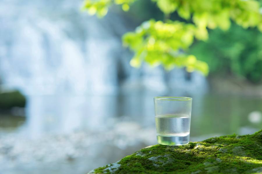 A glass of water next to a mountain spring indicates the concept of artesian water being safe to drink