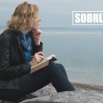 A woman stares out over the ocean with a pad of paper and pen to show the concept of addiction recovery poems