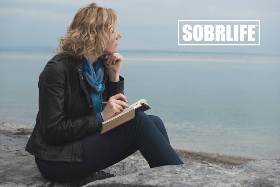 A woman stares out over the ocean with a pad of paper and pen to show the concept of addiction recovery poems